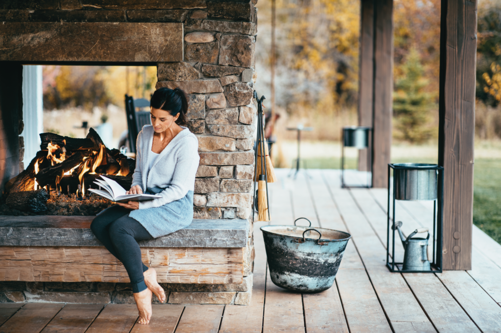 Woman reading a book in front of an outdoor Fireplace